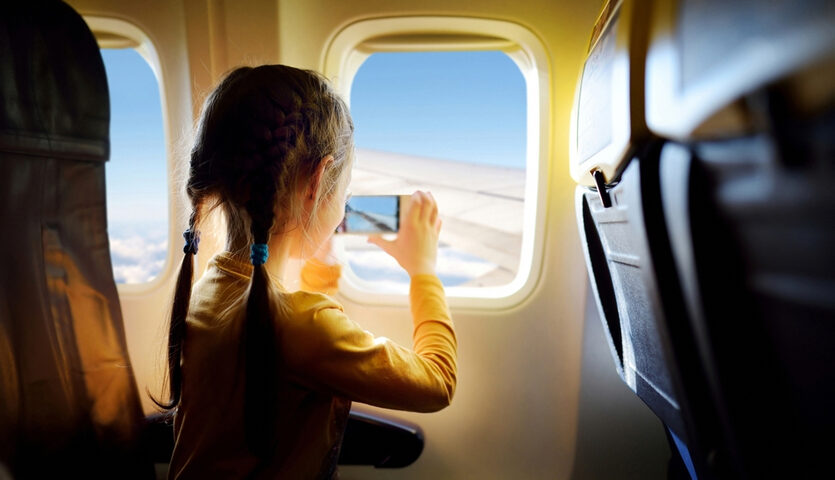MNStudio / Shutterstock girl taking a photo out the window sitting in a window seat on an airplane