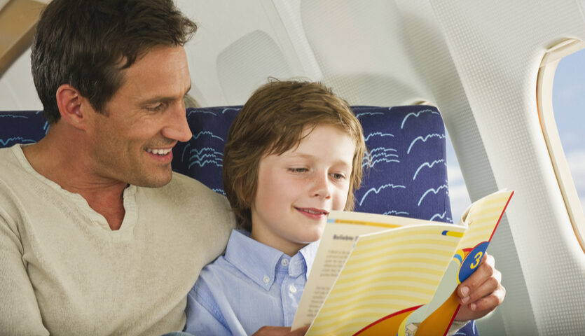 Man sitting next to his son on an airplane while reading